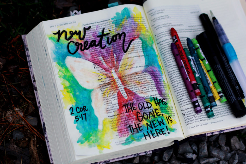 A Bible journaling page of a butterfly. The words New Creation and The old has gone, the new is here are written. The white butterfly is surrounded by a rainbow of colors exploding from behind it.