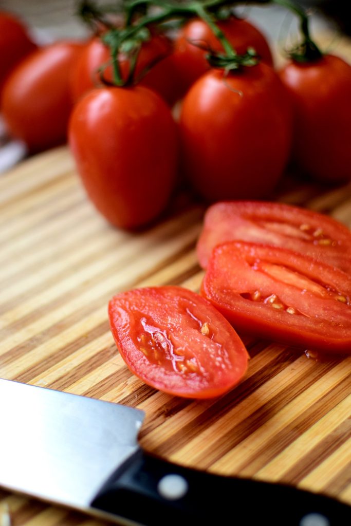 One of the ingredients for a vegan pasta recipe includes juicy red Roma tomatoes that are sliced on a cutting board
