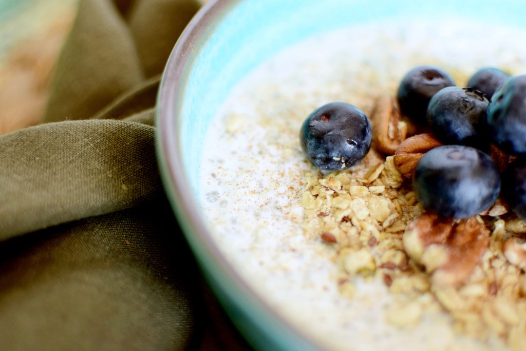 a bright blue bowl of overnight oats topped with granola, pecans, and blueberries