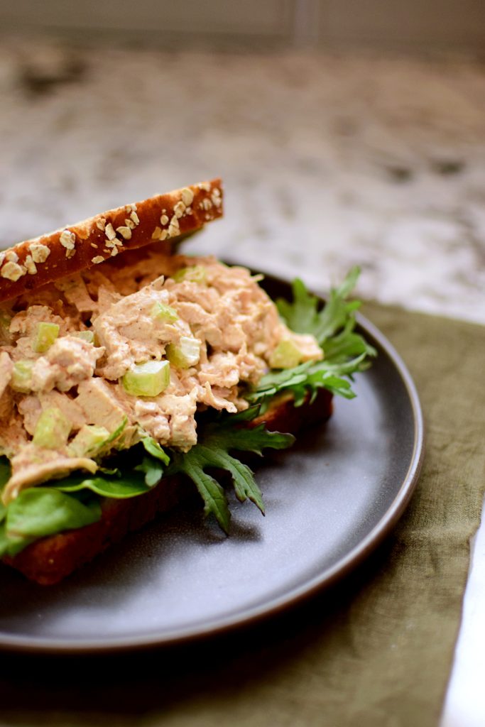 curry chicken salad sandwich on whole grain bread with a bed of greens on a dark gray plate